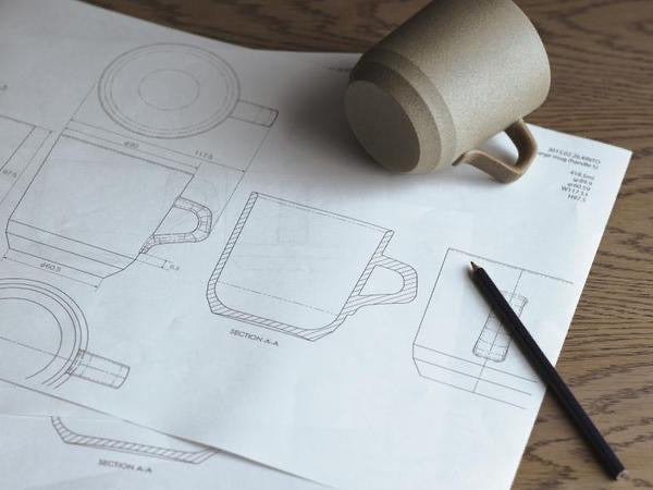 Kinto Ceramic mug on top of blueprints with a pen next to it on a wooden surface